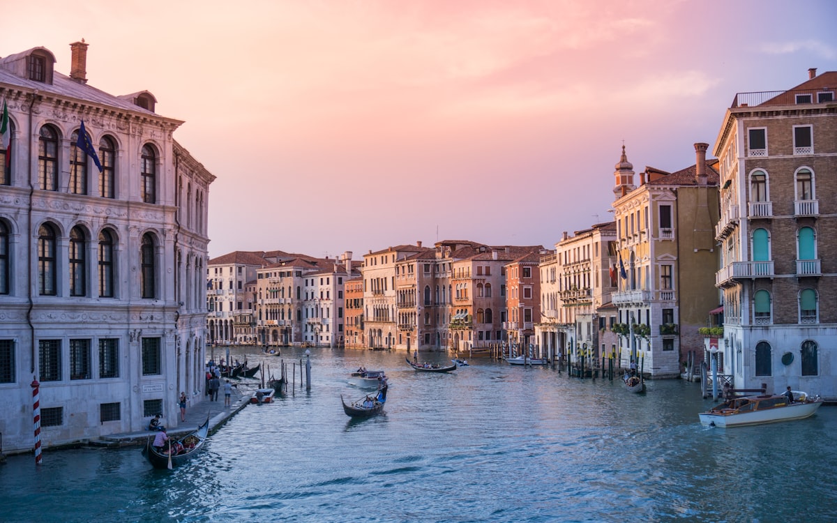 A black gondola gliding through a narrow Venice canal with sunlight reflecting off the water